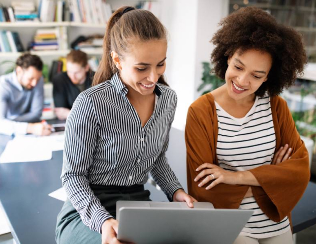 Two women smiling while looking at computer