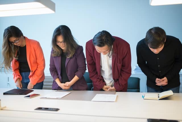 four people standing over a table looking at papers